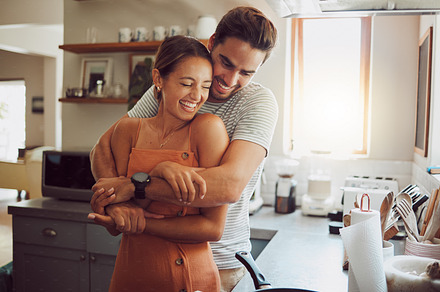 Love, romance and fun with a couple embracing, laughing in a kitchen and sharing an intimate moment. Romantic boyfriend and girlfriend hugging, enjoying their relationship and being carefree together, a Photo by Peopleimages.com