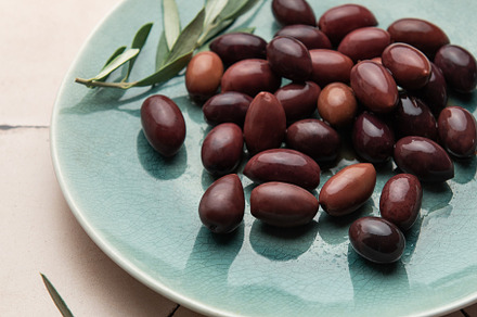 Kalamata olives with olive branches served on a modern plate, a Food & Drink Photo by Olena Rudo