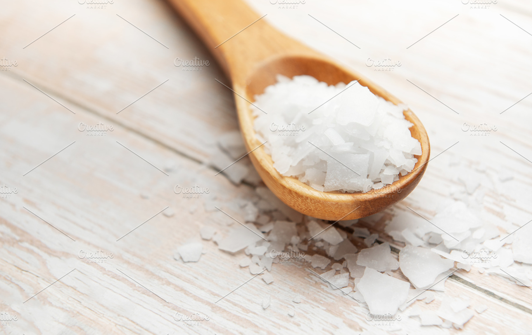 Wooden spoon holding magnesium chloride flakes on white table, a Health & Medical Photo by Olena Rudo