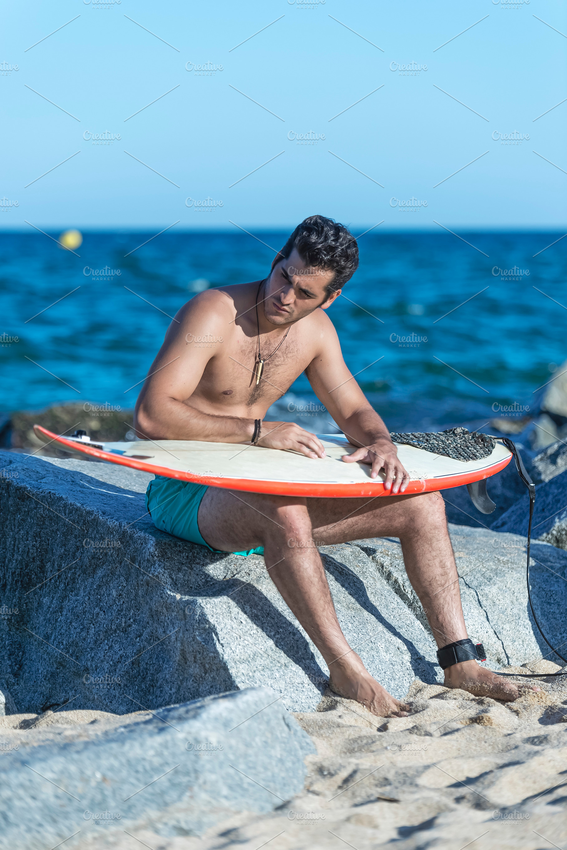 Serious man sitting on rocks with surfboard., a Holiday Photo by 2Design