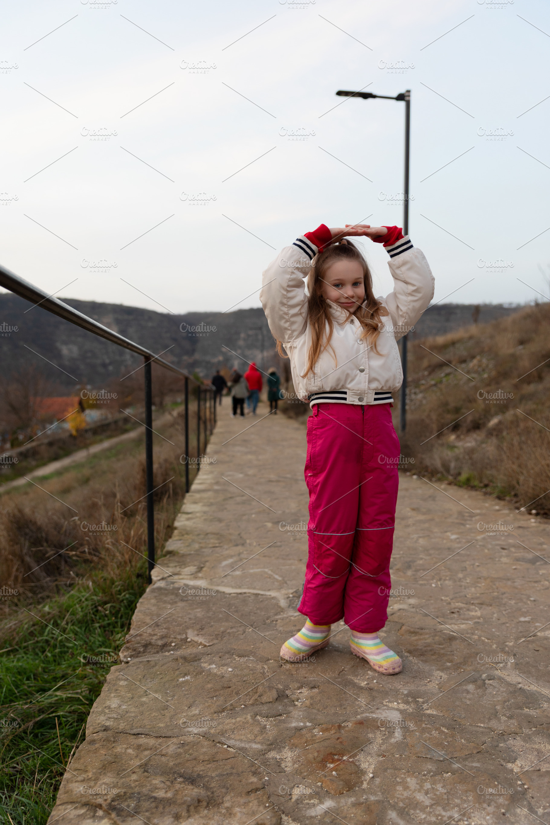 Cheerful young girl in warm clothing poses on a stone path with, a Person Photo by Ales Munt