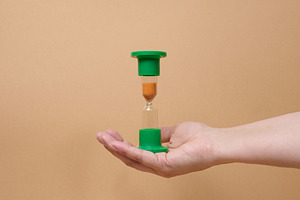 A person holding inverted green hourglass on their palm against, a Business Photo by ndanko