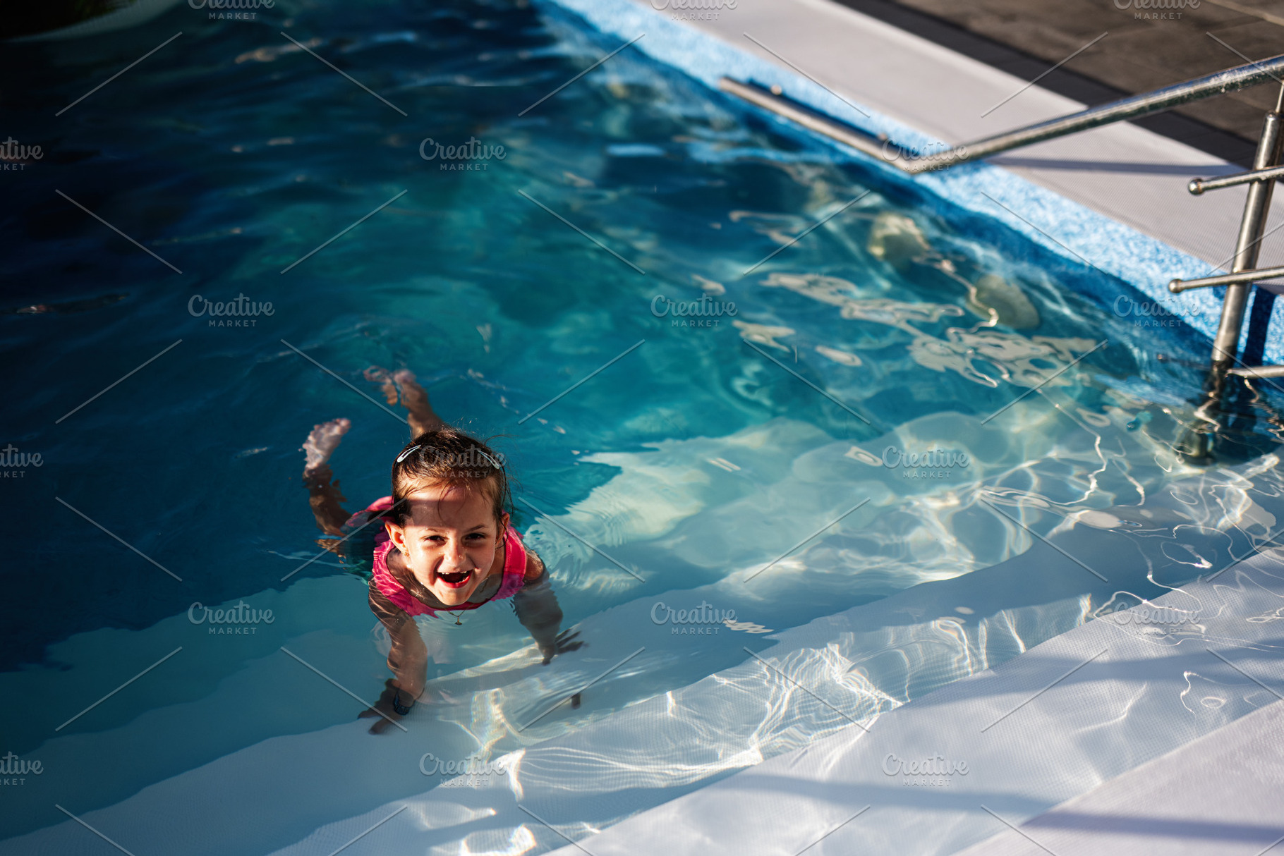 Child swimming and smiling in a clear blue outdoor pool on a sunny day, a Photo by AS photostudio