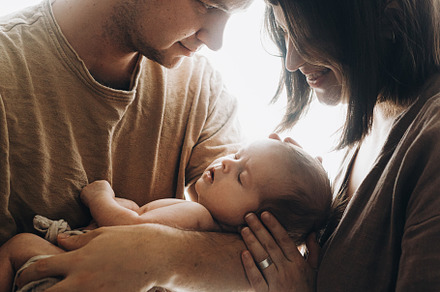 Happy mother and father hugging little baby son in window light.