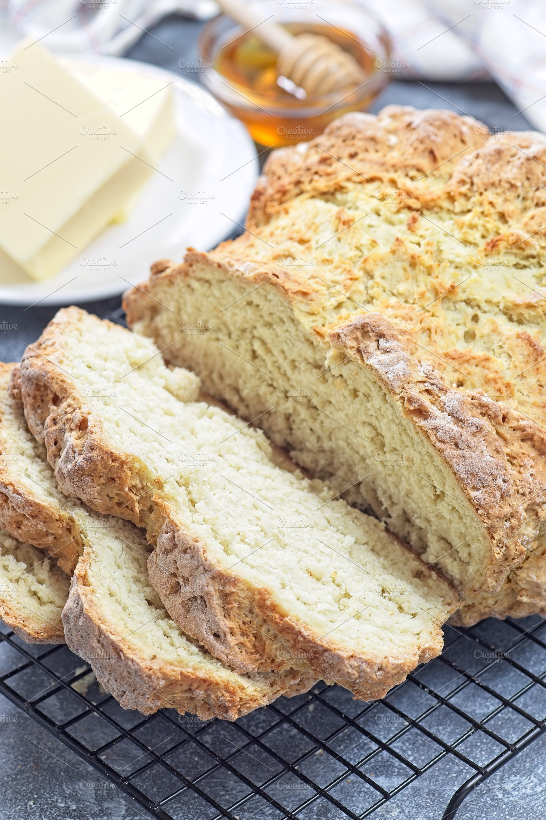 Freshly baked soda bread on cooling rack, sliced, with butter and honey in the, a Food & Drink Photo by iuliia_n