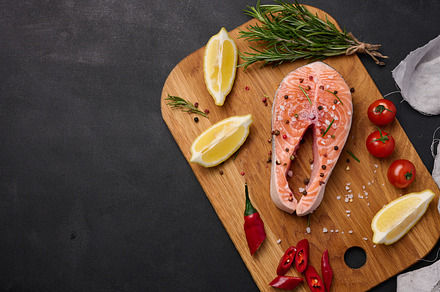 Raw salmon steak on a wooden cutting board, lemon slices, spices, a Food & Drink Photo by ndanko