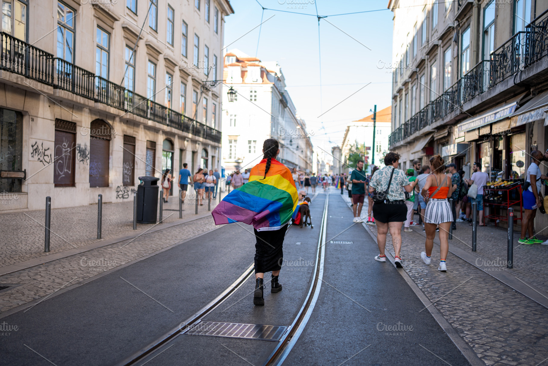 Woman with rainbow flag around her walking on tramway at city street, a Person Photo by andreonegin market