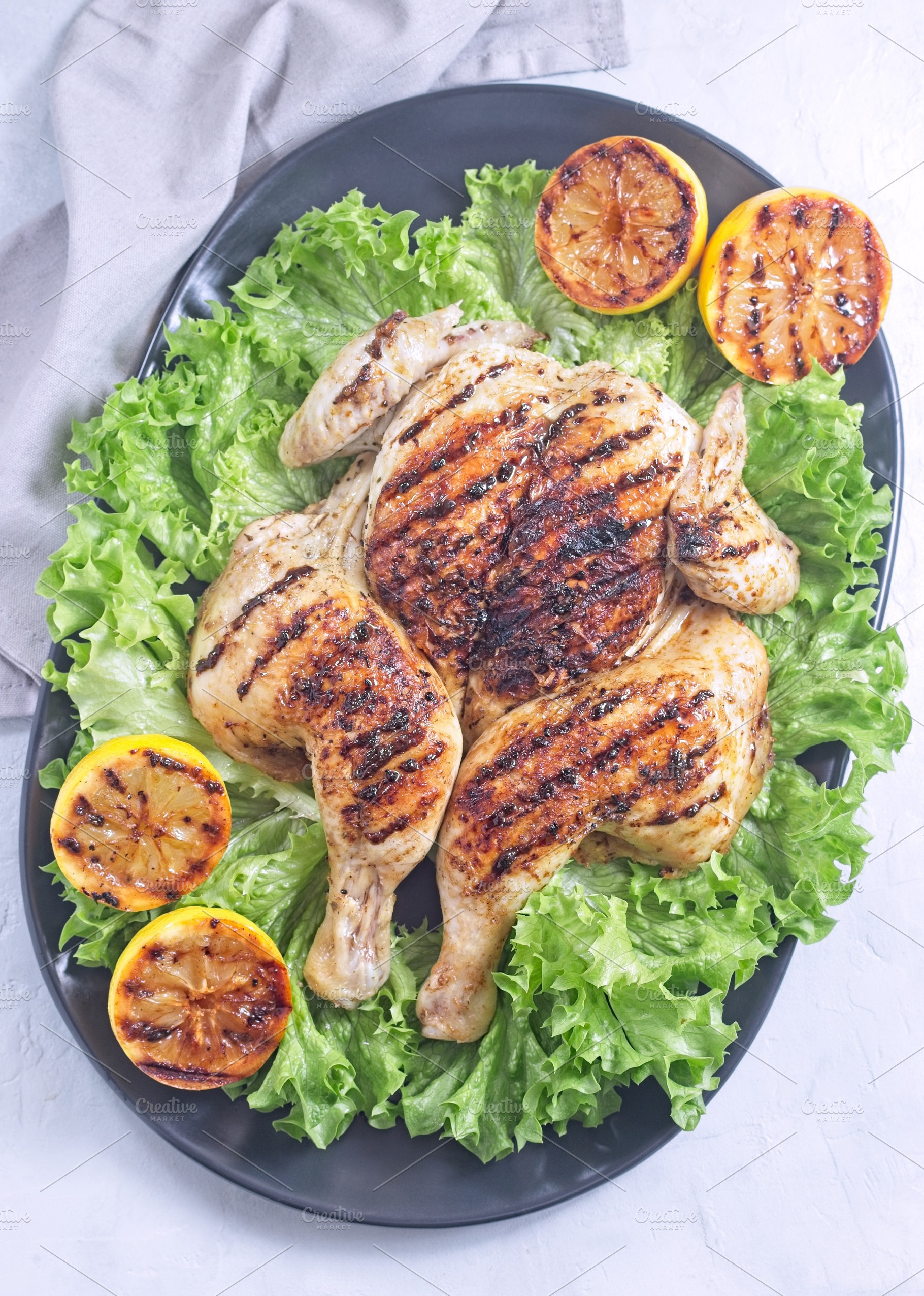 Spatchcocked grilled chicken with lemon garlic marinade on lettuce with lemon,, a Food & Drink Photo by iuliia_n
