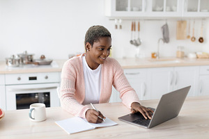 Smiling young african american woman in casual working on laptop in minimalist, a Person Photo by Prostock-Studio