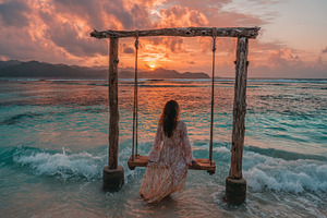 Woman on a swing watching sunset ove, a Photo by Pixeness Studio