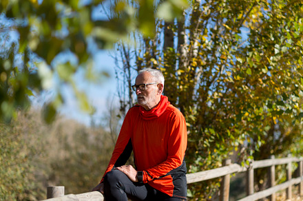Senior man in bright orange hoodie resting on wooden fence