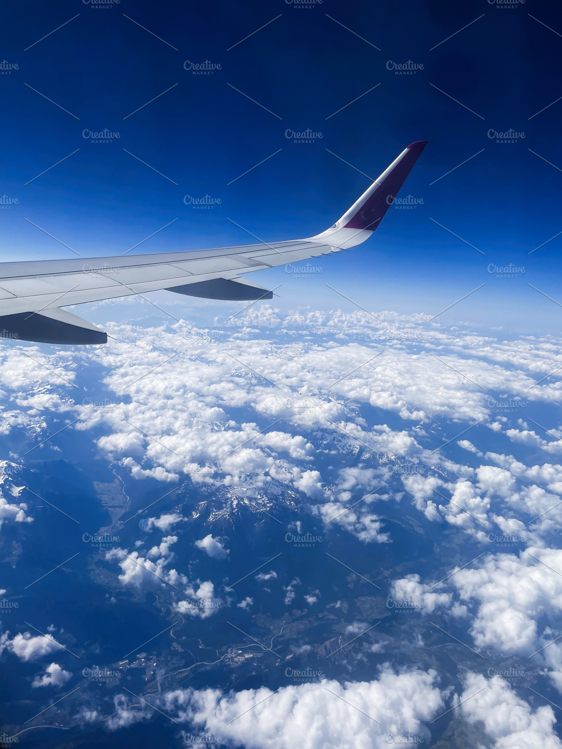 Airplane wing over stunning alpine mountains and fluffy clouds on a sunny day, a Photo by AS photostudio