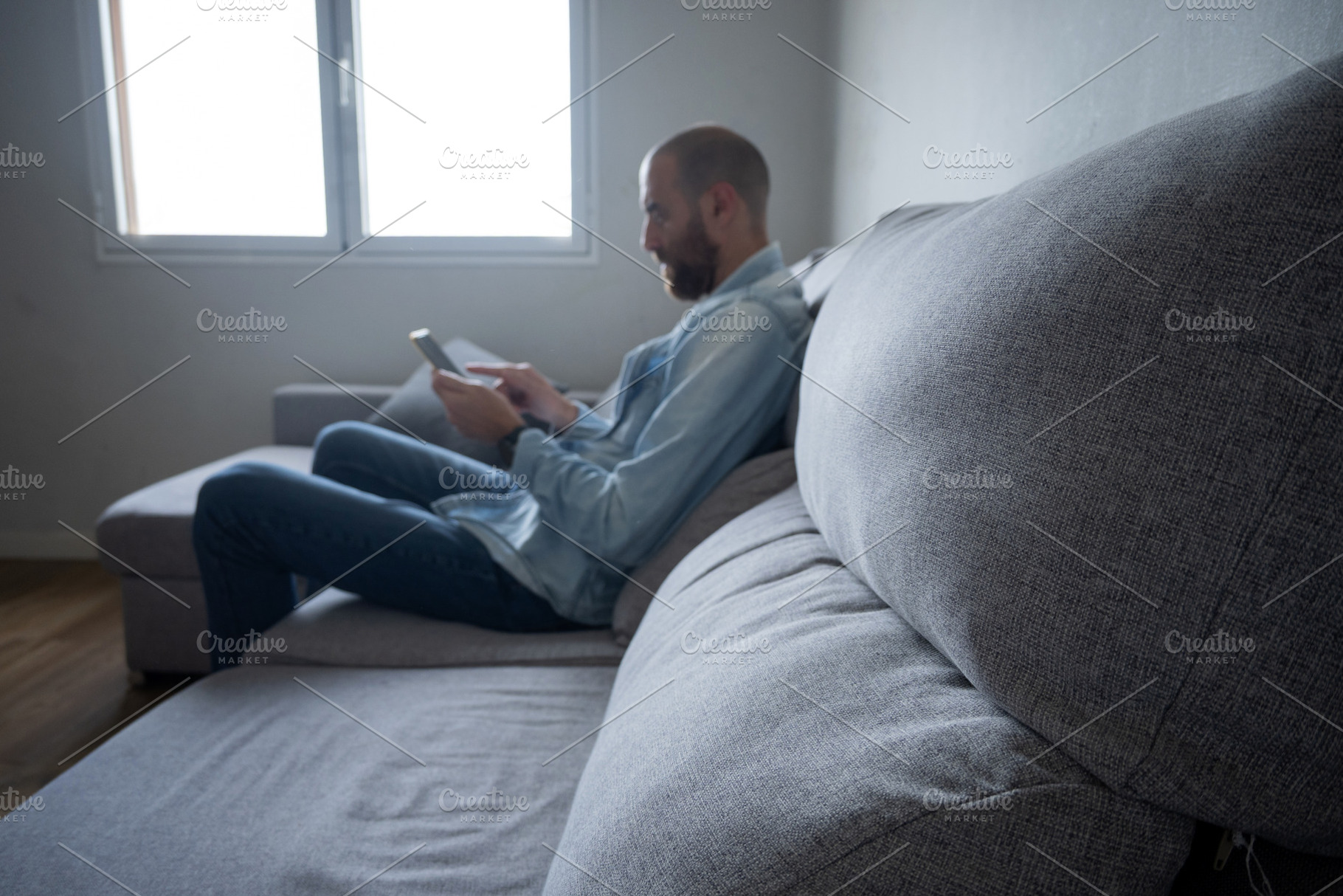 Man using smartphone sitting on sofa at home, relaxed lifestyle with copy space, a Person Photo by etorres69