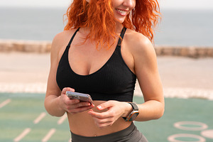Happy sporty woman holding smartphone while standing at outdoor gym, a Person Photo by andreonegin market