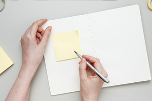 Woman jotting notes on sticky note at tidy workspace surrounded by notebook and, a Photo by matucha