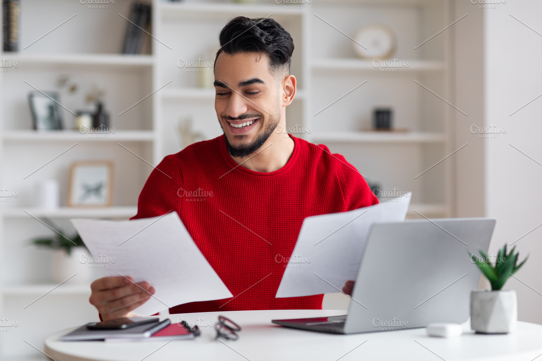 Cheerful young middle eastern man manager with beard works with documents at wo, a Photo by Prostock-Studio