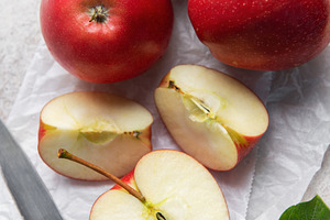 Freshly cut red apples on baking paper with knife and leaves, a Food & Drink Photo by Olena Rudo