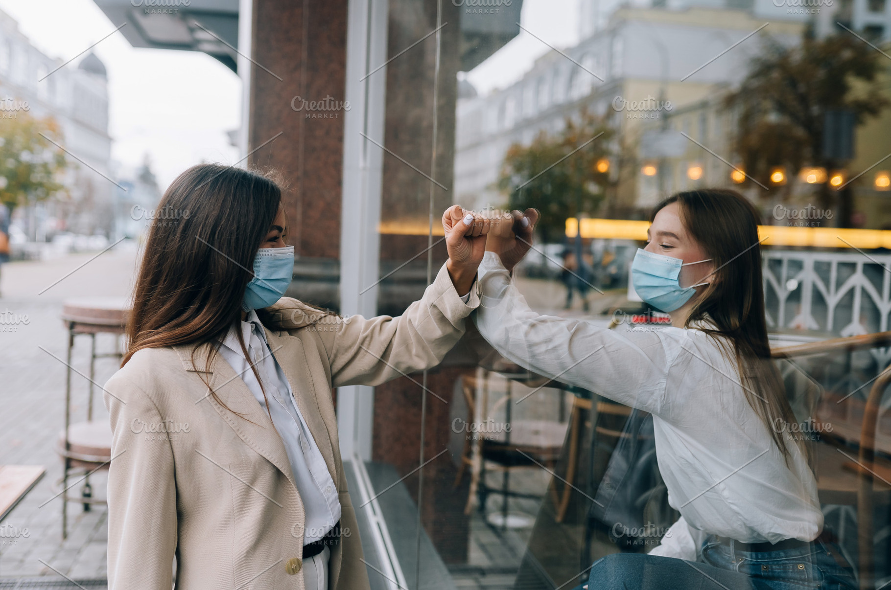 Two women in protective masks opposite each other, window between them., a Person Photo by Tekso