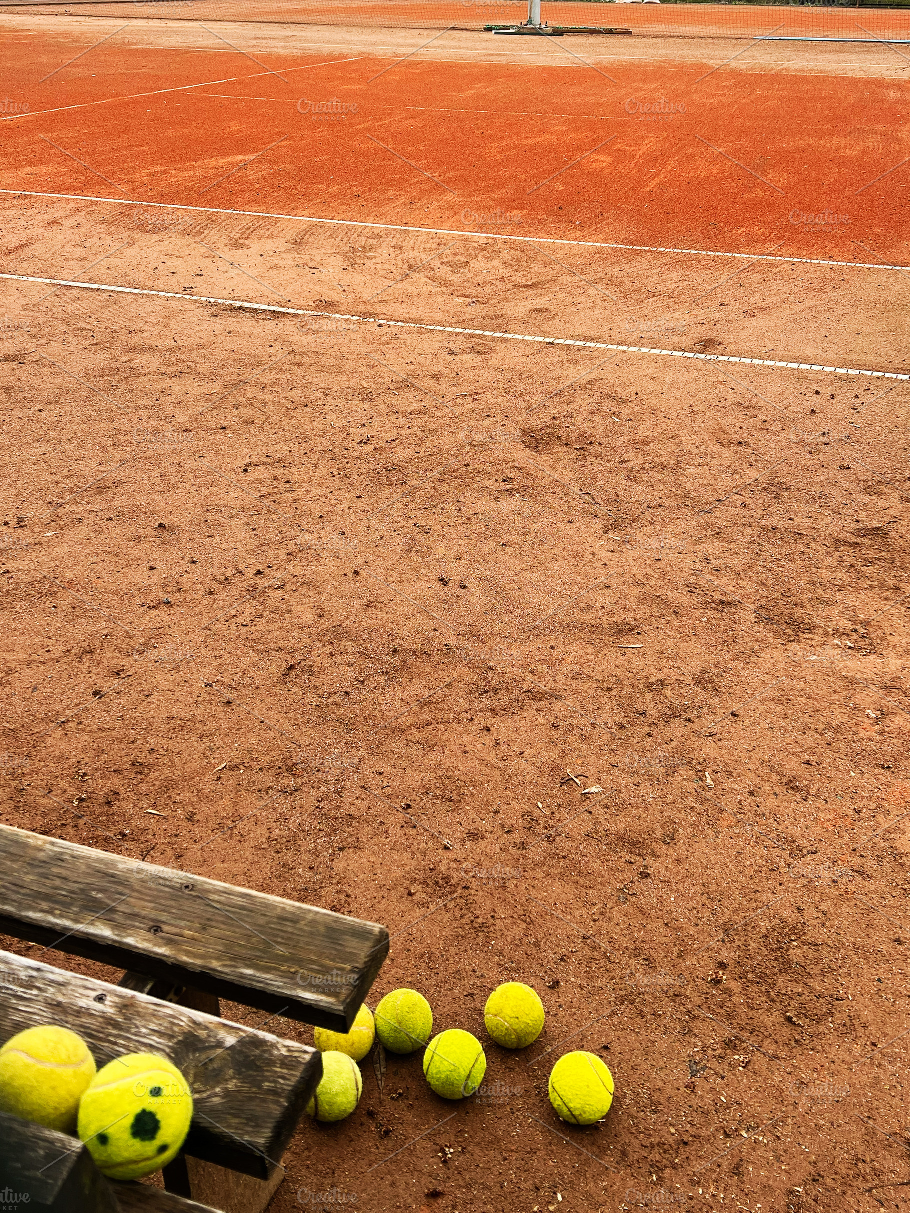Yellow tennis balls scattered on a clay tennis court, a Photo by AS photostudio