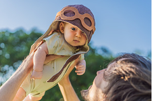 Father lifting baby in a pilot hat, a Holiday Photo by Elizaveta Galitskaya