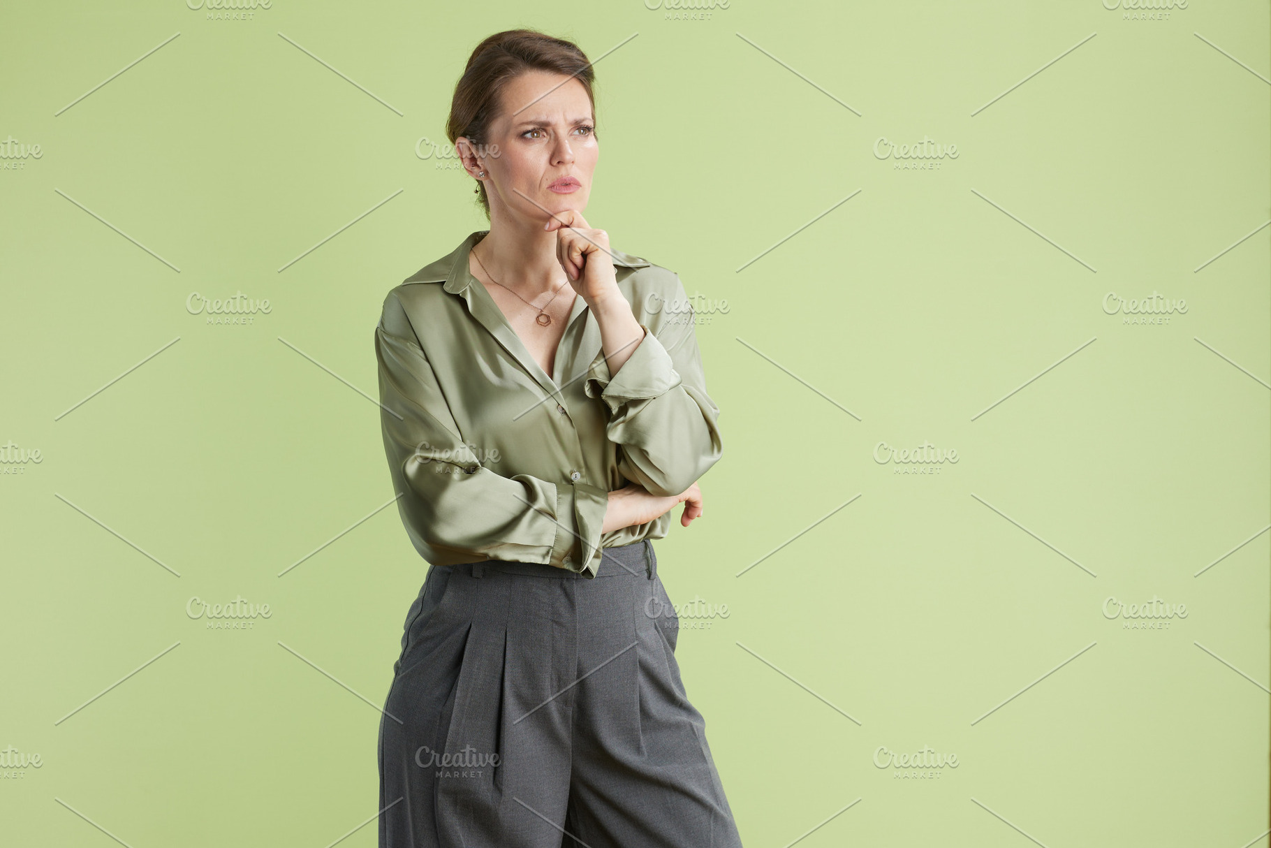 Thoughtful woman in green, hand on chin, a Business Photo by Alliance Images