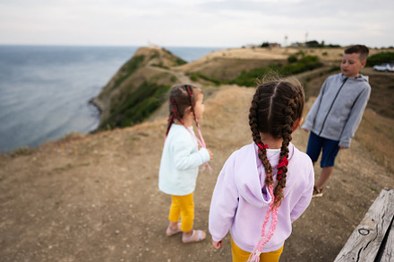 Three kids standing on a cliff and looking at the sea. Sisters w, a Person Photo by AS photostudio