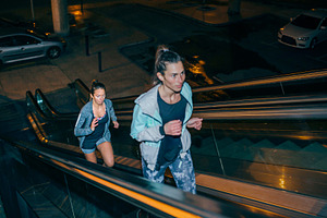 Women friends training running up escalator in city at night, a Sports & Recreation Photo by davidpereiras