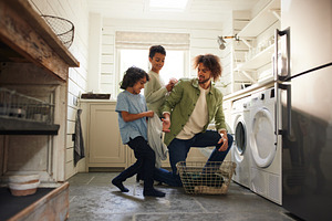 Father and sons loading washing machine in kitchen, a Person Photo by Southworks
