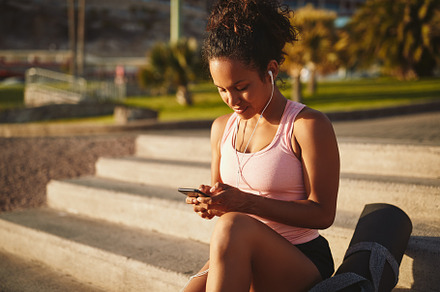 Sporty young woman sitting on park steps using her cellphone