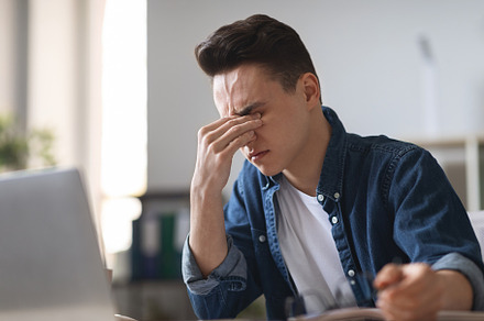 Tired Millennial Guy Suffering Eye Strain While Using Laptop In Office