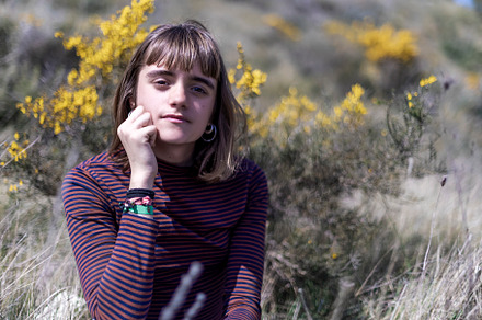 Pretty young woman in sweater sitting on a rock with nature park in background, a Person Photo by 2Design