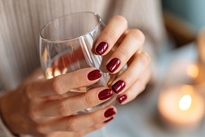 Female hand with five red nails holding a glass of water near candles in a cozy, a Photo by AlyaAnd