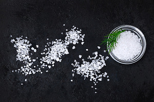 Coarse salt crystals on black table. Bowl with sea salt. Background for adverti