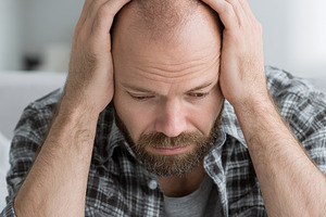 Man sitting on edge of bed with hands on head, displaying signs of stress or wo, a Person Photo by AlyaAnd