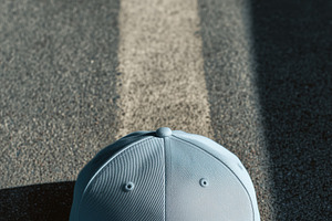 A light blue baseball cap mockup placed on a textured surface with shadows, a Hat Mockup by Textures & Backgrounds