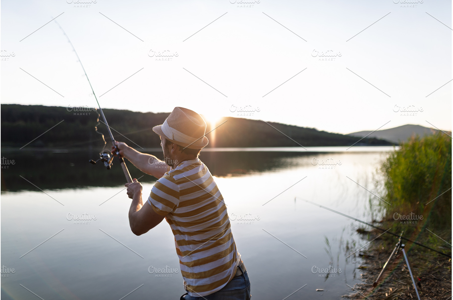 Man fishing by a lake during sunset., a Sports & Recreation Photo by HalfPoint