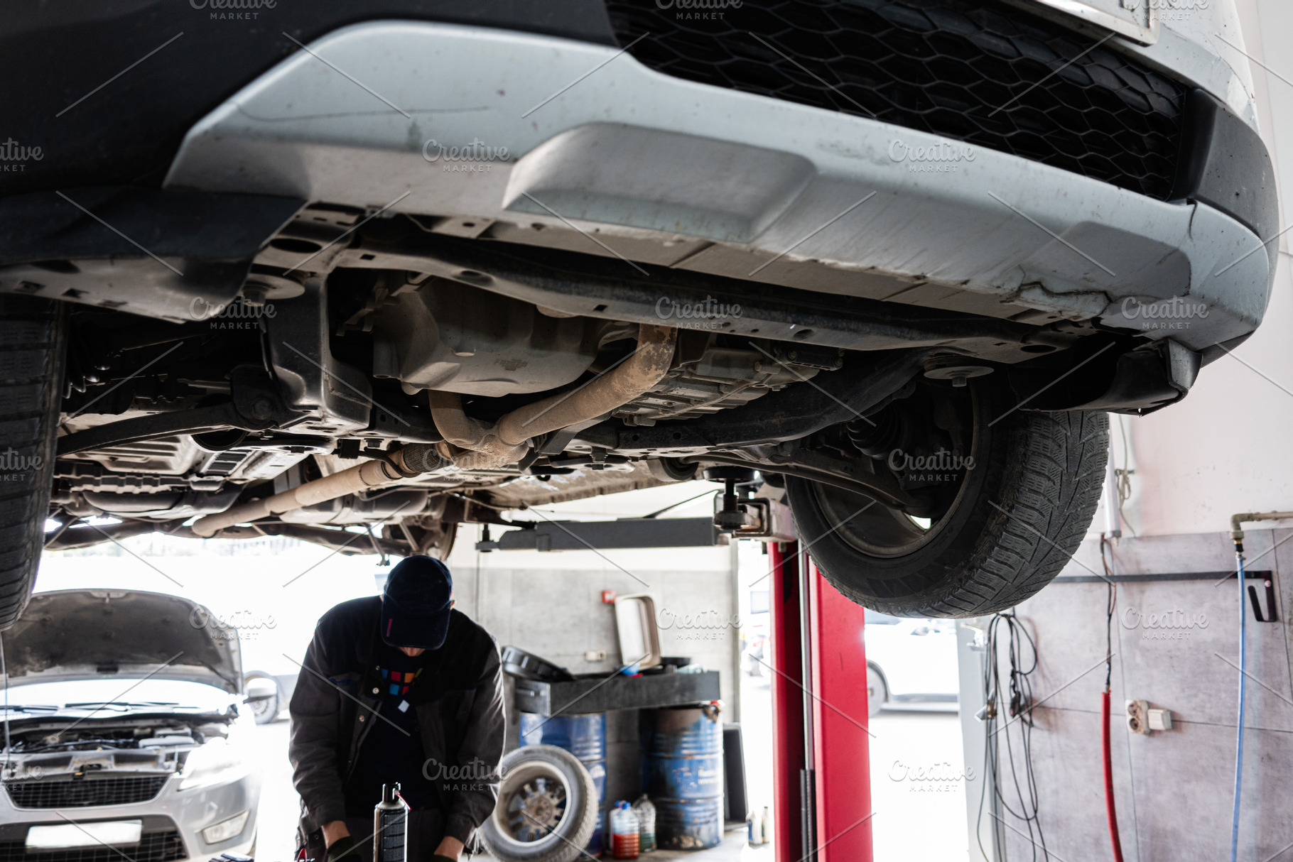 Mechanic inspecting vehicle underside on lift in automobile repair shop, a Transportation Photo by AS photostudio