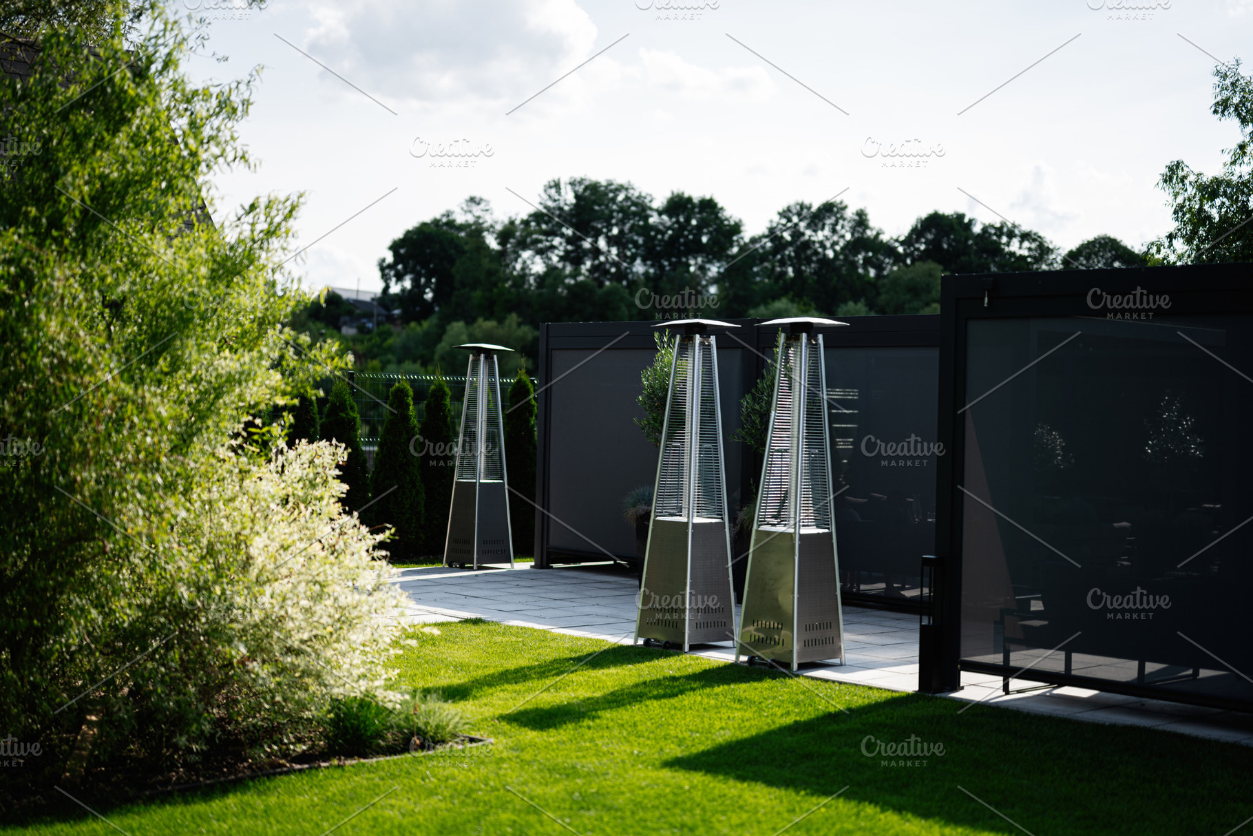 Modern outdoor space with patio heaters and greenery in natural sunlight, a Photo by AS photostudio