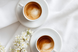Two cups of coffee with spring white flowers on pristine fabric,, a Photo by Studio ANNA