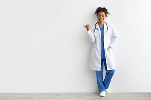 Cheerful female black doctor smiling pointing at copy space, a Photo by Prostock-Studio