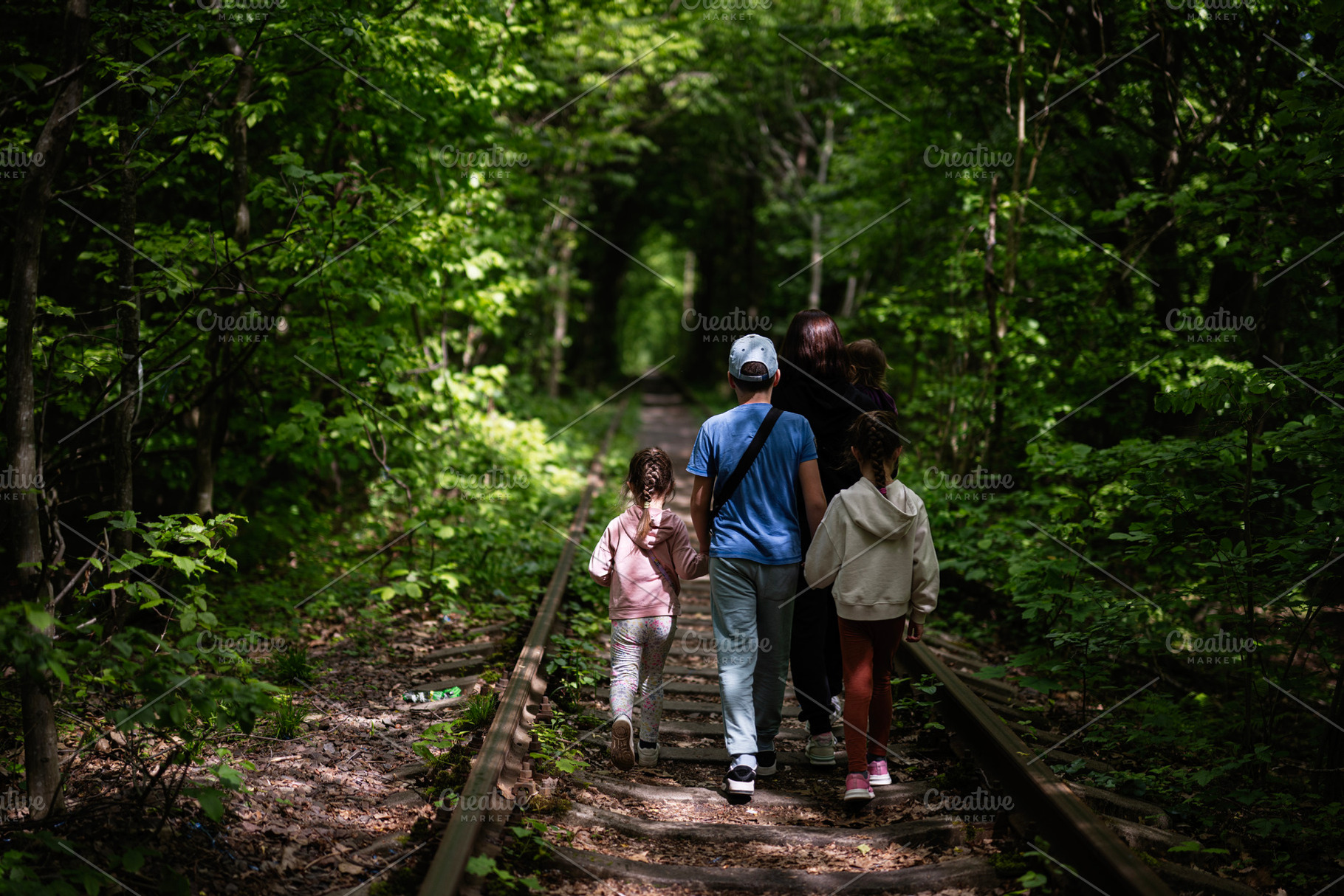 Family walking on abandoned railway tracks in a verdant green forest, a Photo by AS photostudio