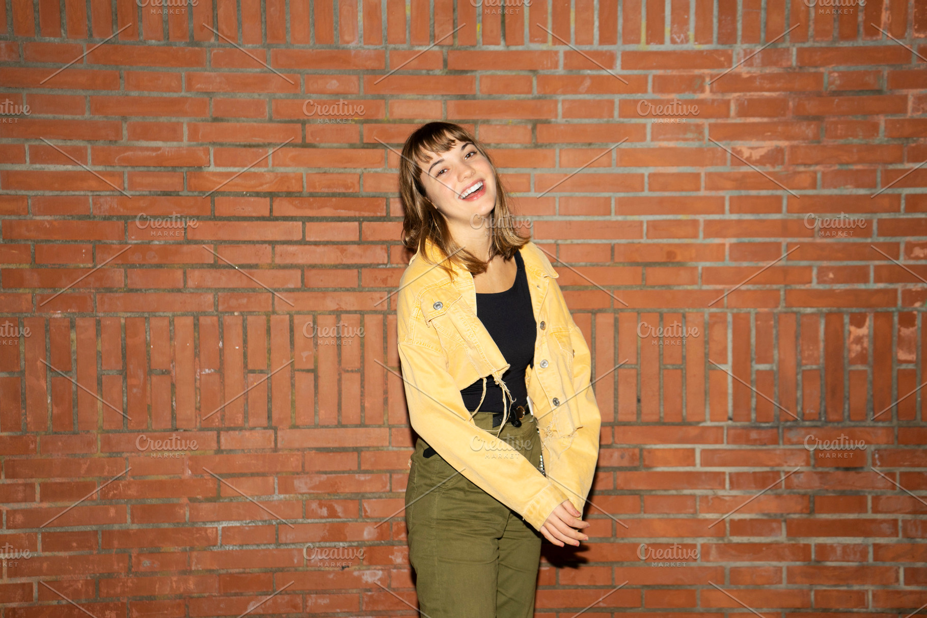 Young woman stands near an old brick wall in the city at night, a Person Photo by 2Design