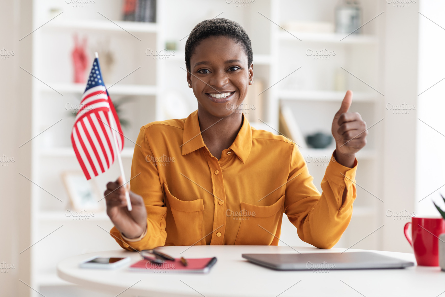Positive african american woman showing flag of USA, thumb up, a Photo by Prostock-Studio