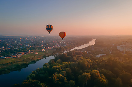 Two colorful air balloons flying over green park and river in small european ci
