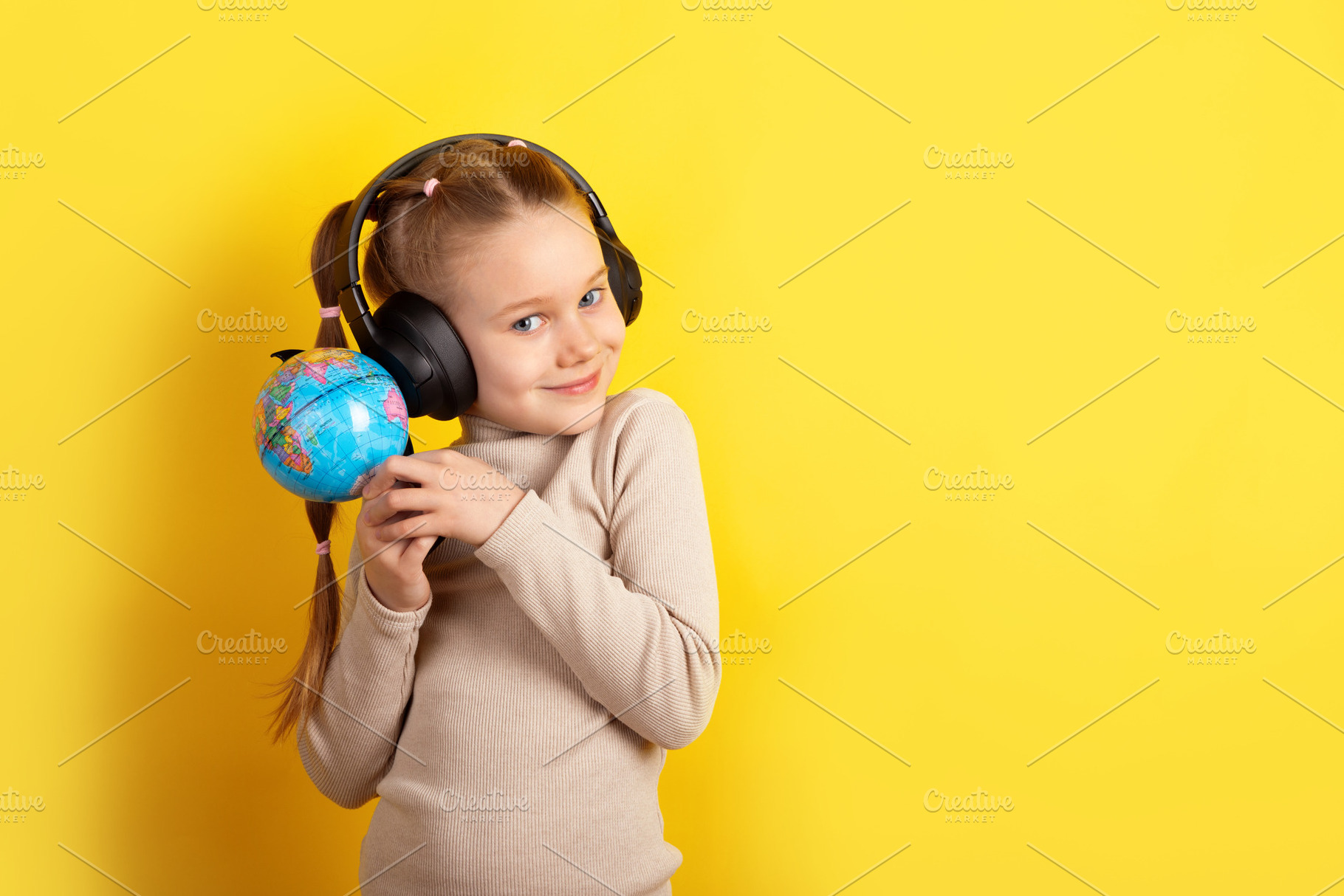Smiling young girl holding a small globe and wearing headphones,, a Person Photo by Ales Munt