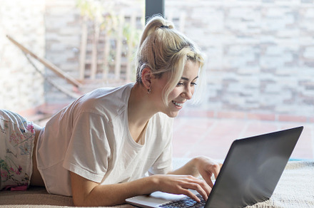 Photo of young joyful woman in pajama typing on laptop and smiling while lying, a Person Photo by 2Design