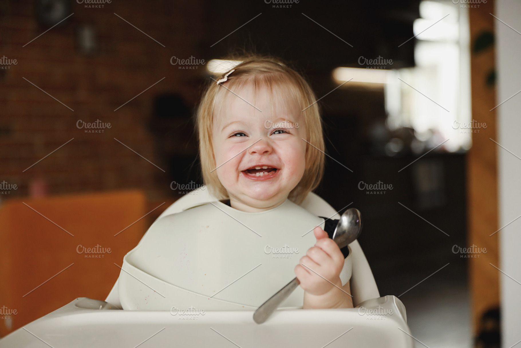 Infant girl or toddler sitting on high chair. Eating food by herself using spoo, a Person Photo by Lenor4ik