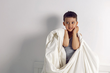 child boy is mad having fun in a white bed in the children's room with a blanke, a Person Photo by SaulichPhoto