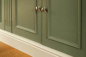 Green wooden cabinet with panel doors and brass knobs, white baseboard accentin, a Photo by Studio ANNA