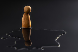 A wooden peg doll stands alone, staring down at its reflection i, a Photo by salmon.black